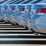 A close up of the rear bumpers on a line of sedans is shown at a buy here pay here car lot.
