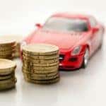 Three stacks of coins are shown in front of a red die-cast car.