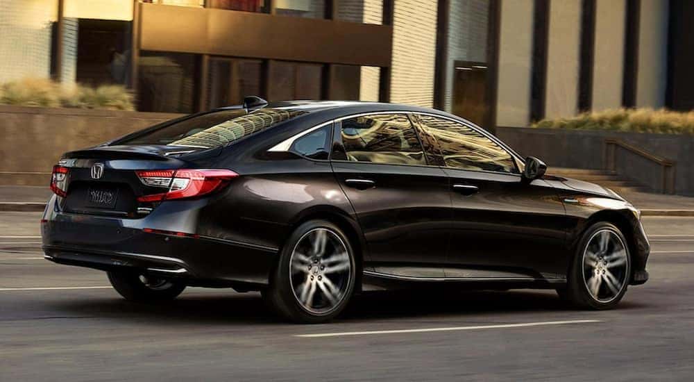 A 2021 crystal black pearl Honda Accord Hybrid shown from the side is driving through an urban area.