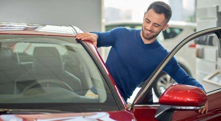 A smiling man is shown getting into a red car at a Belton, MO buy here pay here dealership.