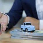 A close up shows a hand holding a key and a toy car on top of money.