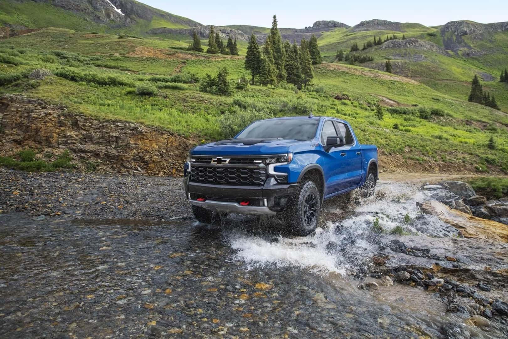 Chevrolet Silverado driving through shallow river in the mountains splashing up water around tires
