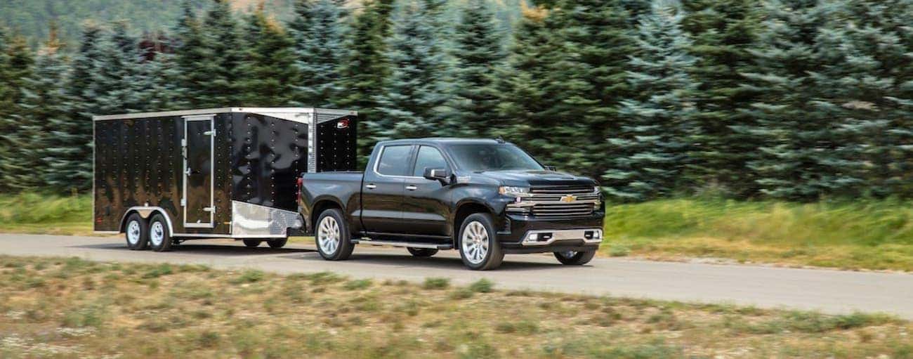 A black 2020 Chevy Silverado 1500 is towing a black enclosed trailer past pine trees.