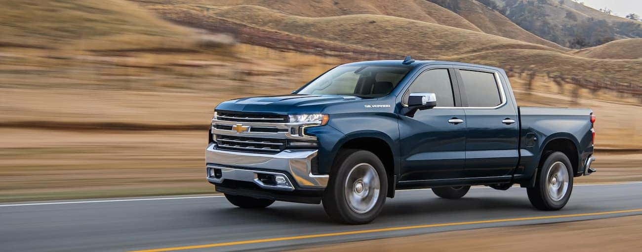 A blue 2020 Chevy Silverado 1500 is driving past blurred hills outside Indianapolis, IN.