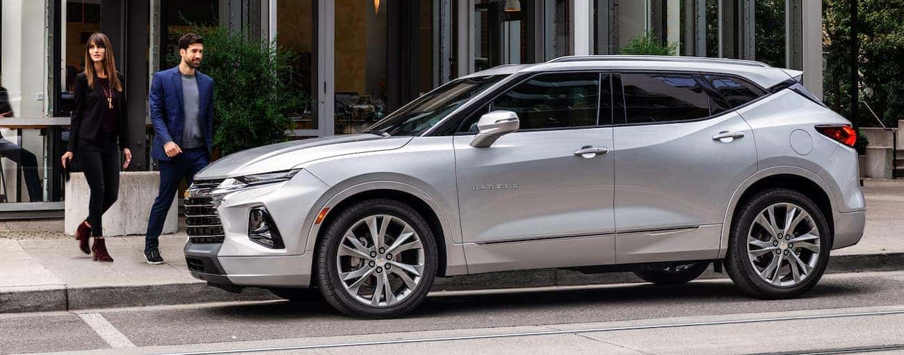 A couple is walking toward a silver 2020 Chevy Blazer parked on a city street.