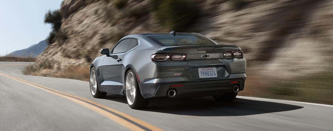 A grey 2020 Chevy Camaro is driving on a road lined with rock face.