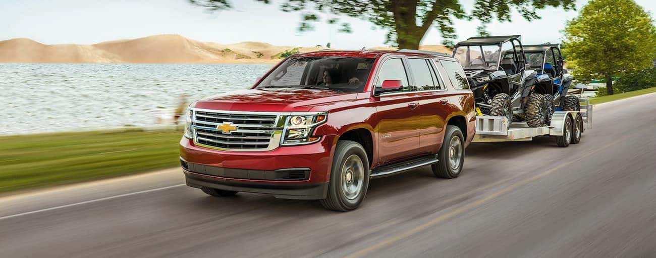 A red 2020 Chevy Tahoe is towing side-by-sides past a lake.