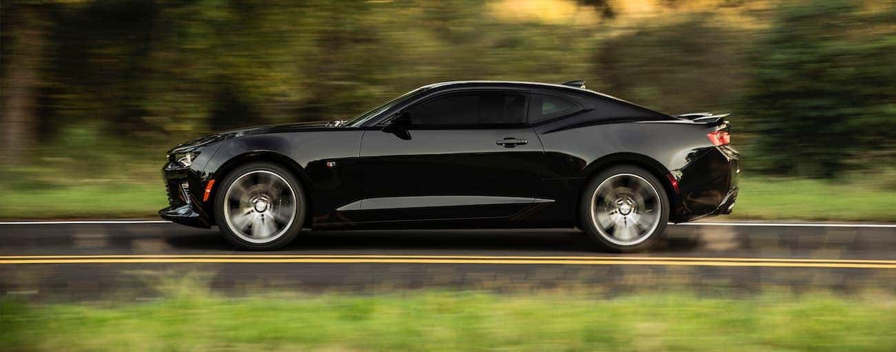 A black 2016 used Chevrolet Camaro is shown driving from the side on a tree-lined road.