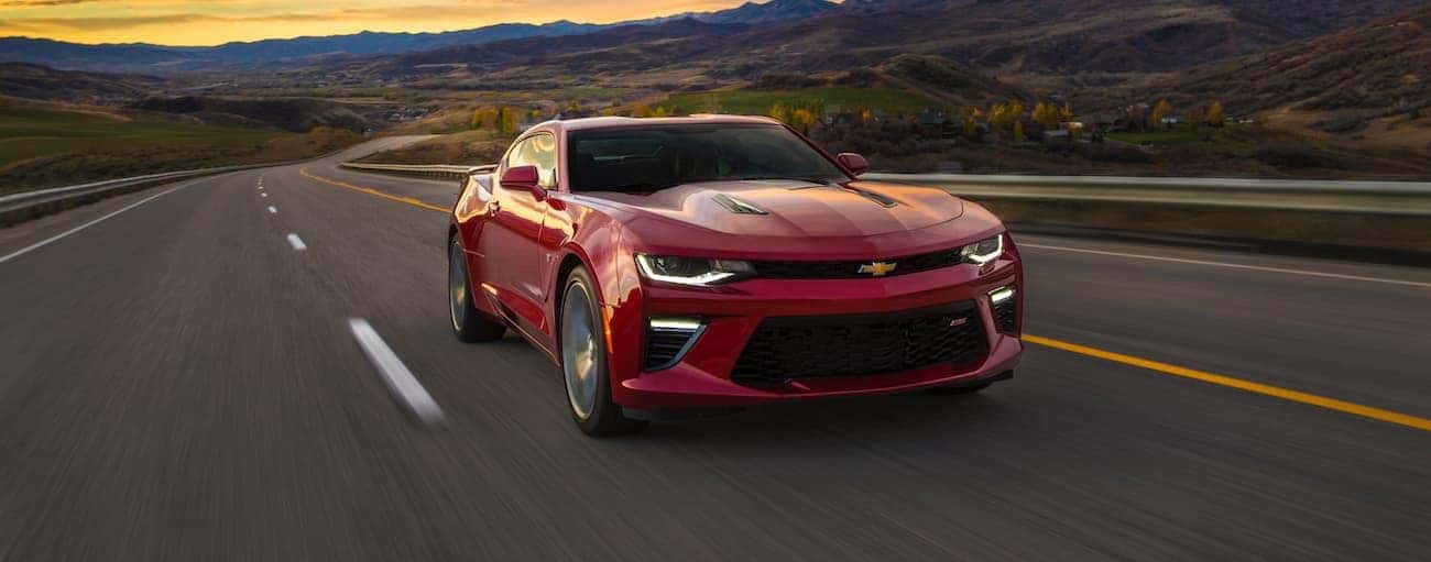 A red 2017 used Chevrolet Camaro is driving on a highway at sunset with mountains in the distance.
