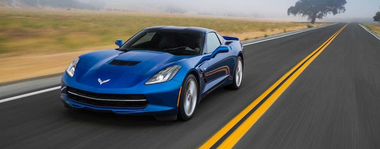 A blue 2016 used Chevrolet Corvette is driving past a field outside of Indianapolis, IN.