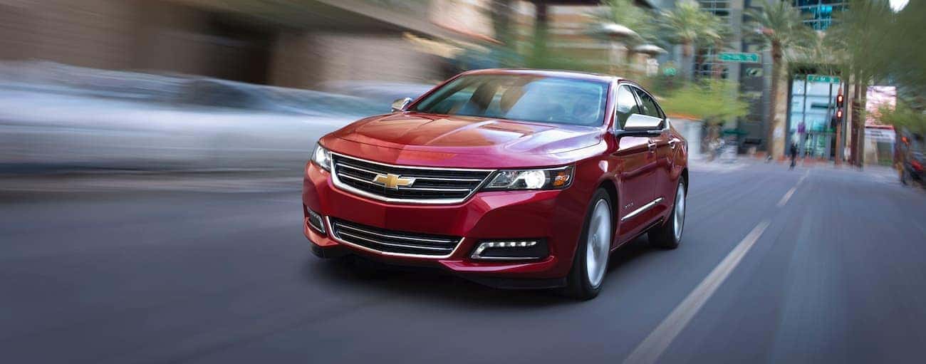 A red 2016 used Chevrolet Impala is driving on a city street near Indianapolis, IN.
