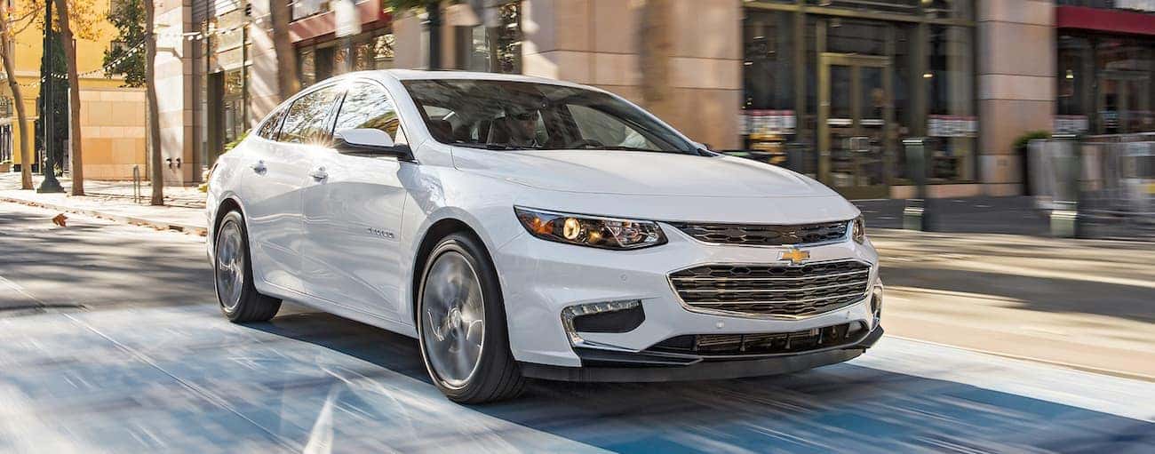 A white 2016 used Chevrolet Malibu is driving through an intersection in Indianapolis, IN.