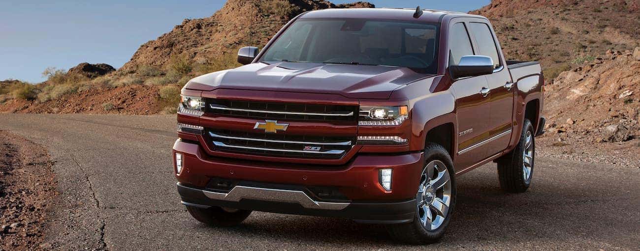 A red 2017 Used Chevrolet Silverado 1500 is parked on a road in front of desert rocks.