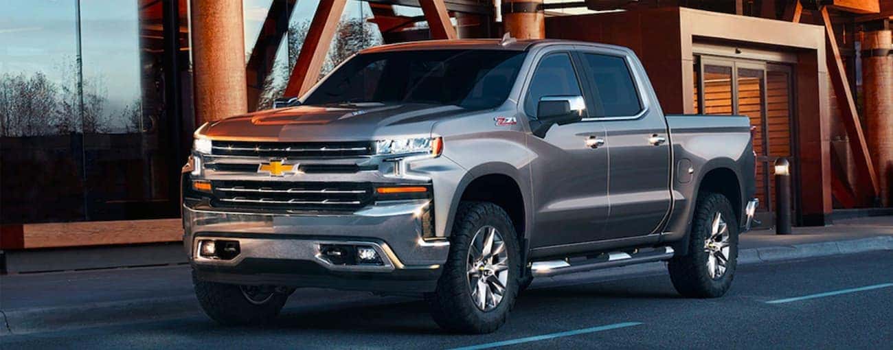 A grey 2019 Used Chevrolet Silverado 1500 is parked in front of a glass and wood building near Indianapolis, IN.