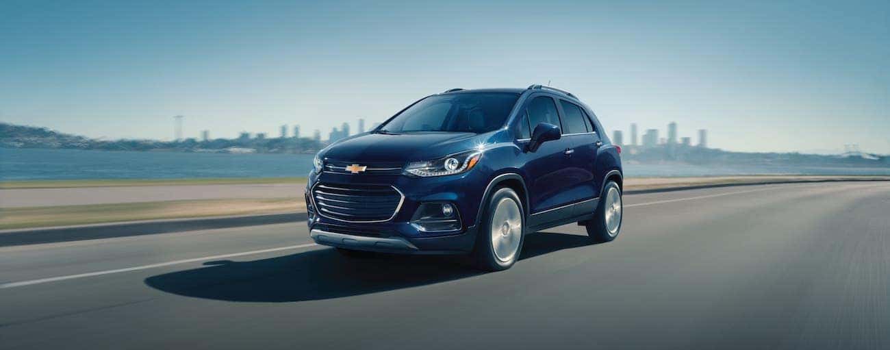 A dark blue 2018 used Chevrolet Trax is driving away from a city.