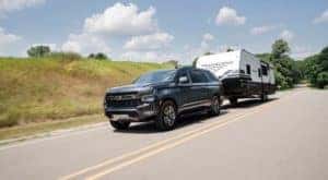 A newer Chevy SUV, a gray 2021 Chevy Suburban Z71, is towing a trailer on a highway near Indianapolis, IN.