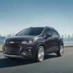 A gray 2020 Chevy Trax is driving away from a Chevrolet Dealer near Lawrence, Indiana, and away from a city.