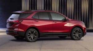 A red 2022 Chevy Equinox from a Chevy Dealer near Lawrence, Indiana, is parked in front of a stylish wall and shown from the side.