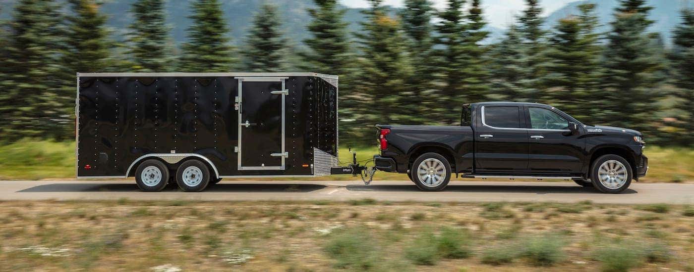 A black 2021 Chevy Silverado 1500 High Country is shown from the side while towing a black enclosed trailer.
