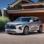 A silver 2021 Chevy Blazer is flanked by a man and woman parked in front of a modern house.