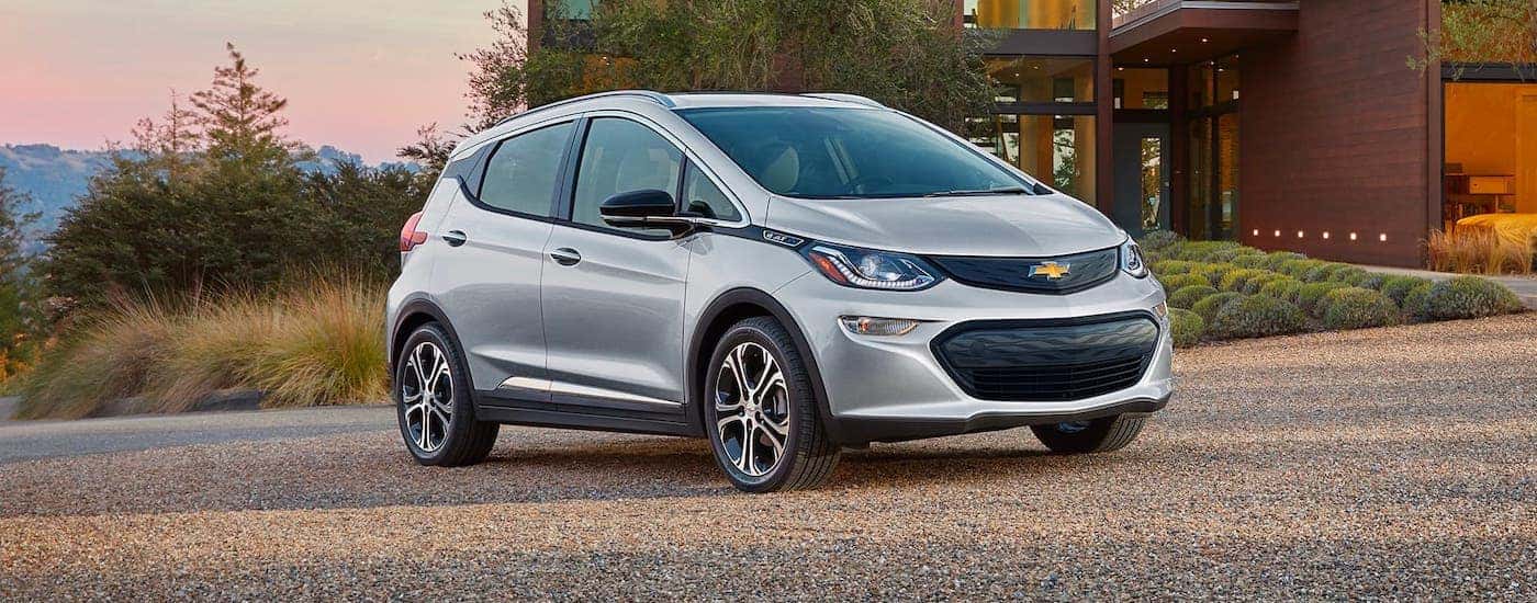 A silver 2021 Chevy Bolt EV is parked in front of a modern home at dusk.
