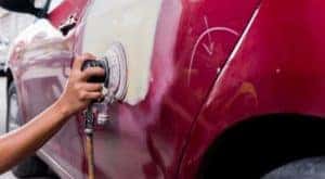 A mechanic is sanding a section of a red car that has received body work.