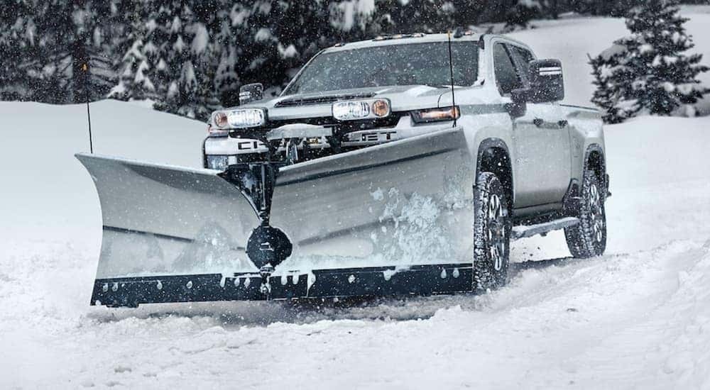 A white 2021 Chevy Silverado 2500 HD with a plow is in a snow storm.