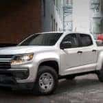 A popular Chevy commercial vehicle, a white 2021 Chevy Colorado, is shown angled left while parked in the city.