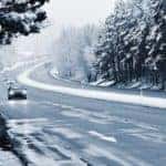 A snowy two lane highway is shown with cars commuting.
