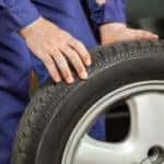 A close up shows a mechanic rolling a tire and rim.