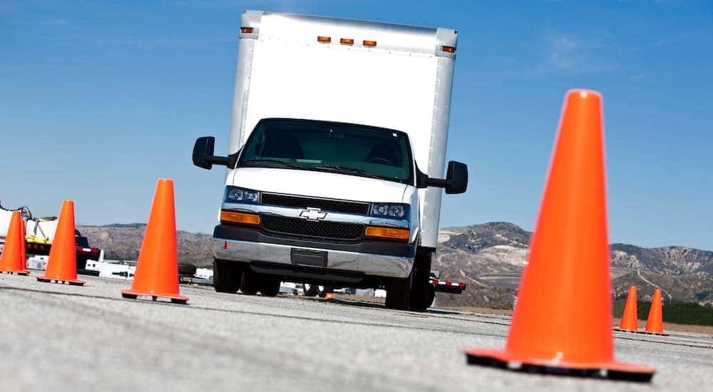 A white 2016 Chevy Express 4500 Cutaway is shown from a low angle surrounded by orange cones.