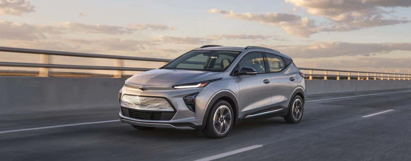 A silver 2022 Chevy Bolt EUV is driving on a highway close to sunset.