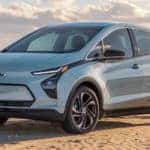 A light blue 2022 Chevy Bolt EV is parked on beach sand.