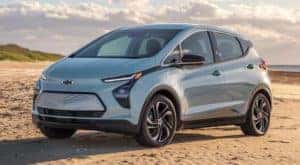 A light blue 2022 Chevy Bolt EV is parked on beach sand.