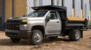 A silver 2021 Chevy Silverado 3500 Chassis Cab with a dump body is parked at a building site.