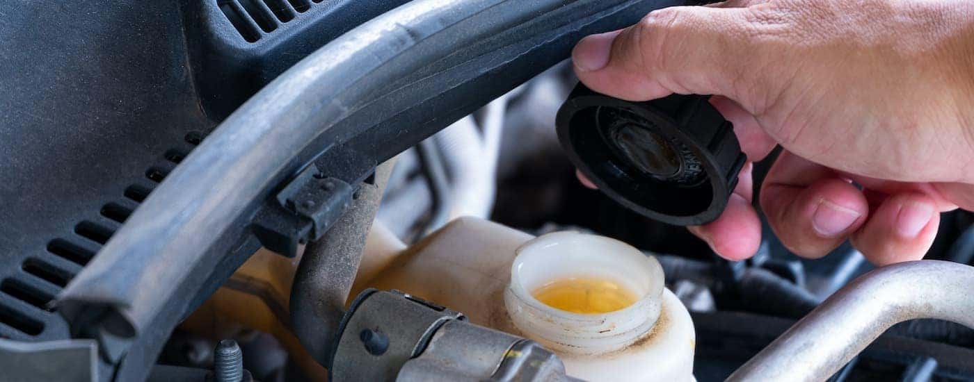 A close up shows a hand removing a brake fluid reservoir cap during a brake service.