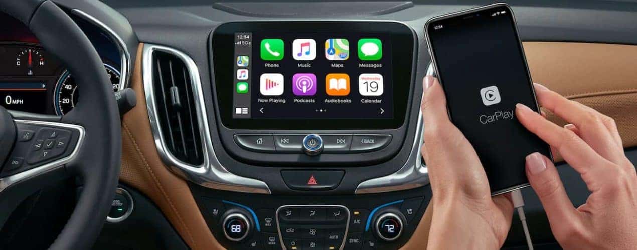 A phone with CarPlay on the screen is in front of the 2021 Chevy Equinox infotainment screen with app icons displayed.