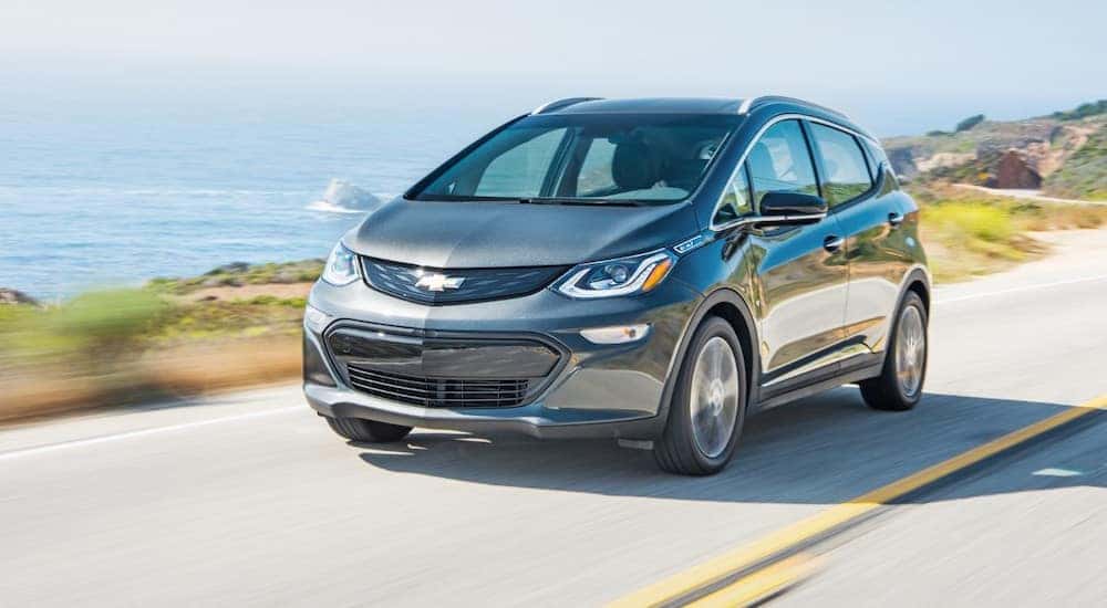 A gray 2019 Chevy Bolt EV is shown driving on a highway near a body of water.