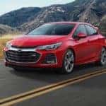 A red 2019 Chevy Cruze is shown driving past a lake with a mountain view.