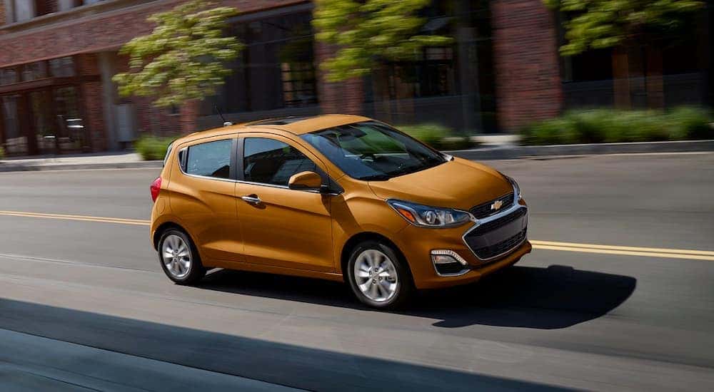 An orange 2020 Chevy Spark is shown driving after visiting a pre-owned car dealer in Indianapolis.