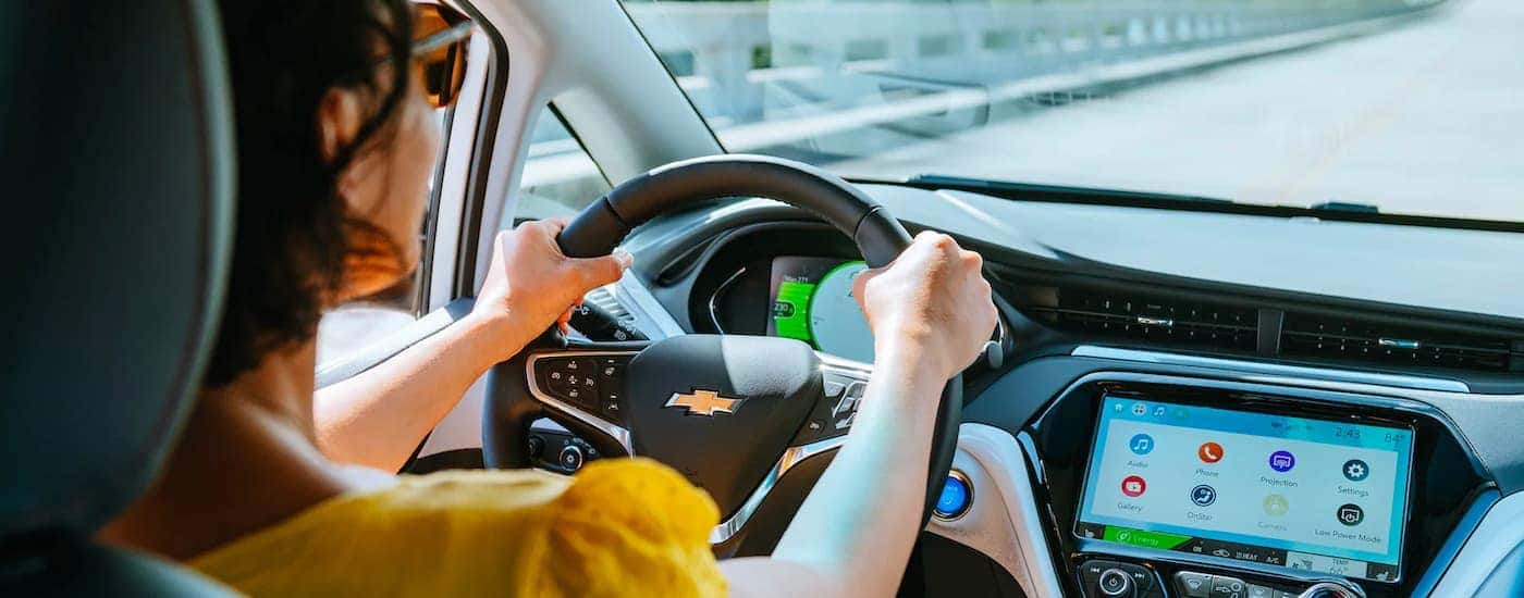 A woman in sunglasses is shown driving a 2020 Chevy Bolt EV.