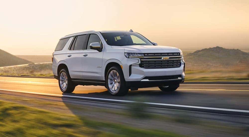 A white 2022 Chevy Tahoe is shown from the side driving on an open road at sunset.