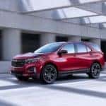 A red 2022 Chevy Equinox RS is shown from the side while it drives down a covered highway after leaving a Carmel Chevrolet dealership.