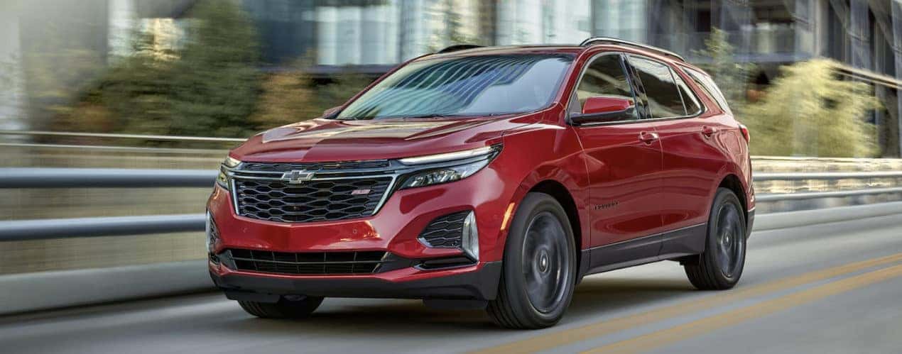 A red 2022 Chevy Equinox is shown from the front driving past a city.