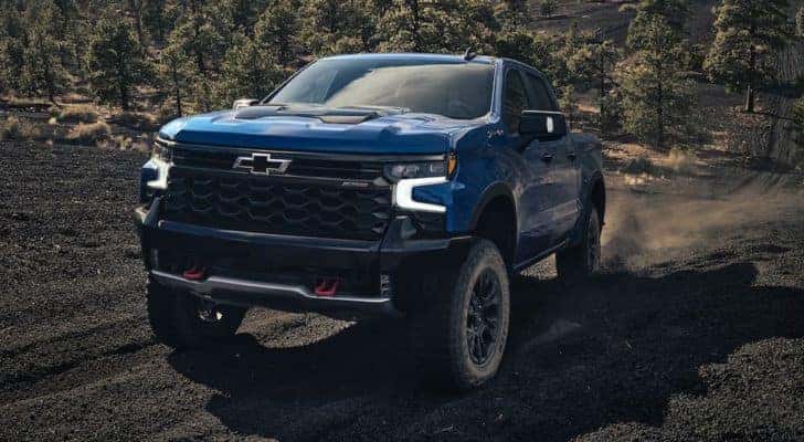 A blue 2022 Chevy Silverado 1500 ZR2 is shown driving up a dirt path after visiting an Avon Chevrolet dealer.