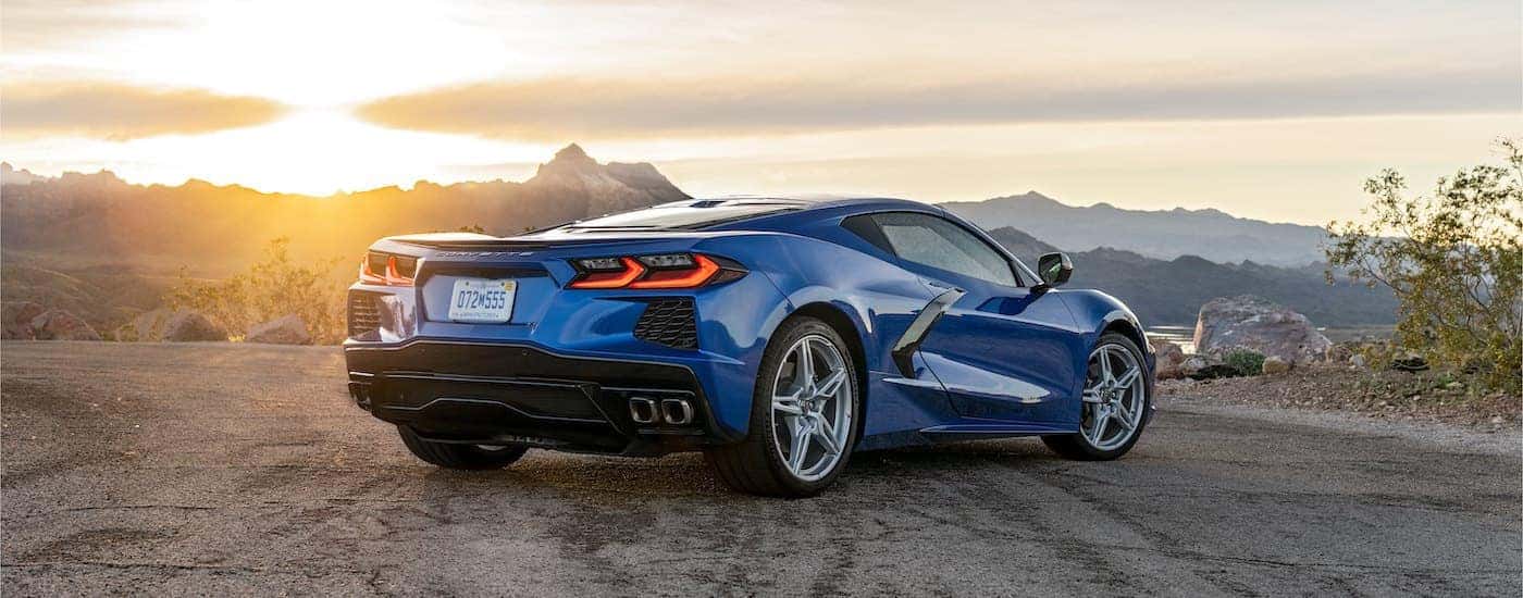 A blue 2022 Chevy Corvette Stingray is shown from a rear angle parked on gravel.