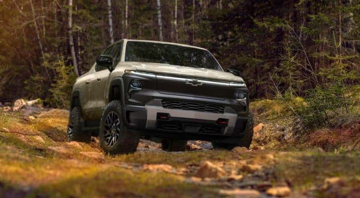 A tan 2024 Chevy Silverado EV Trail Boss is shown from the front parked in the woods.