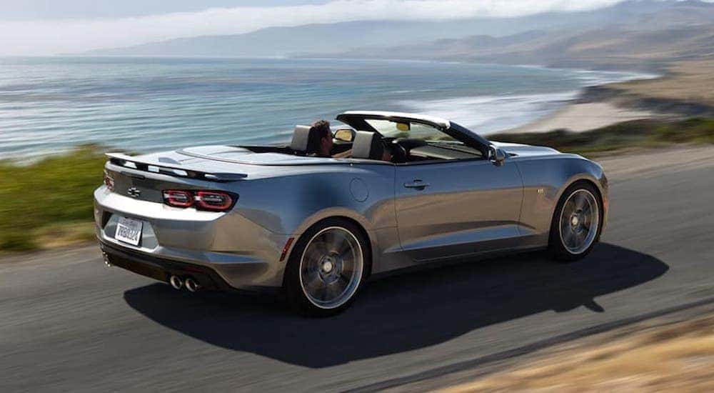 A silver 2021 Chevy Camaro is shown driving down a lakeside road.