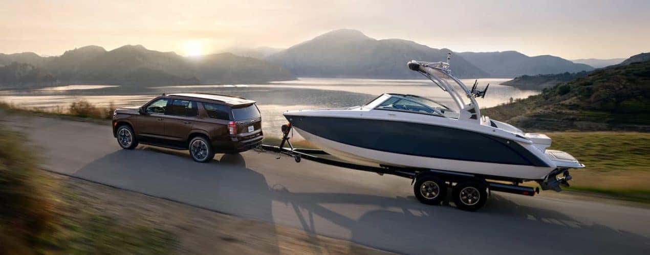A brown 2023 Chevy Tahoe RST is shown towing a boat.