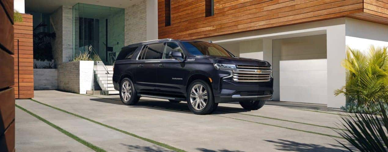 A blue 2023 Chevy Suburban is shown from the side parked in front of a house.